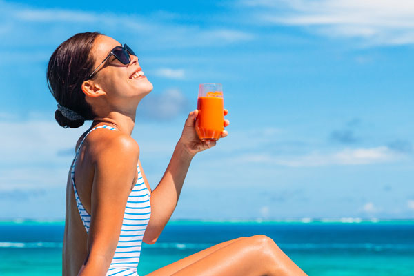 Une femme au soleil entrain de boire un jus de carotte