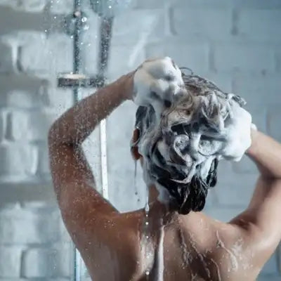 Une femme sous la douche se nettoyant les cheveux.