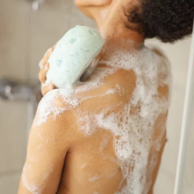 Personne se lavant le dos sous la douche avec un savon solide moussant, pour illustrer l’hygiène corporelle naturelle.