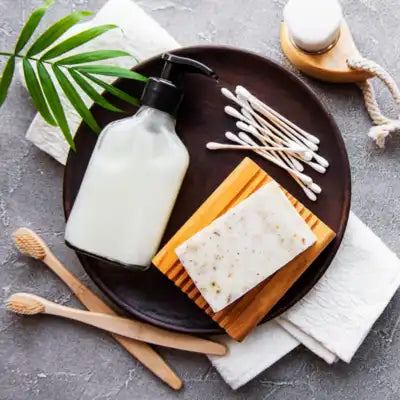 Produits d’hygiène naturels avec savon, brosse à dents, cotons-tiges et flacon, présentés sur un plateau avec une feuille verte.