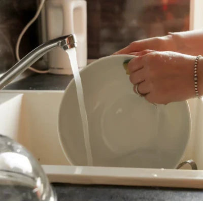 Personne rinçant une assiette sous l’eau du robinet, pour illustrer le lavage de la vaisselle au quotidien.