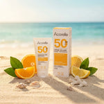Crème solaire Acorelle SPF50 bio sur plage avec agrumes et feuilles vertes