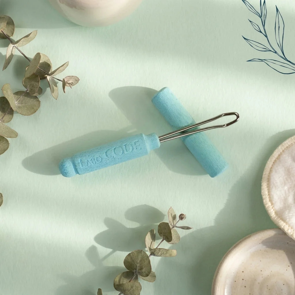 Cure-oreille réutilisable Laboratoire Code avec manche bleu et cuillère inox sur fond vert sauge