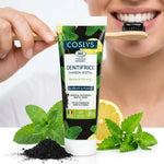 Dentifrice charbon végétal Coslys bio appliqué sur brosse à dents avec feuilles de menthe
