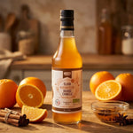 Élixir Orange-Cannelle bio en bouteille avec oranges fraiches et bâtons de cannelle sur plan de travail