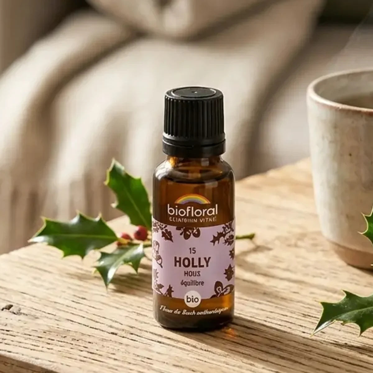 Fleur de Bach Holly (Houx) Bio en granules : flacon ambré sur table en bois, plaid, tisane et branches de houx