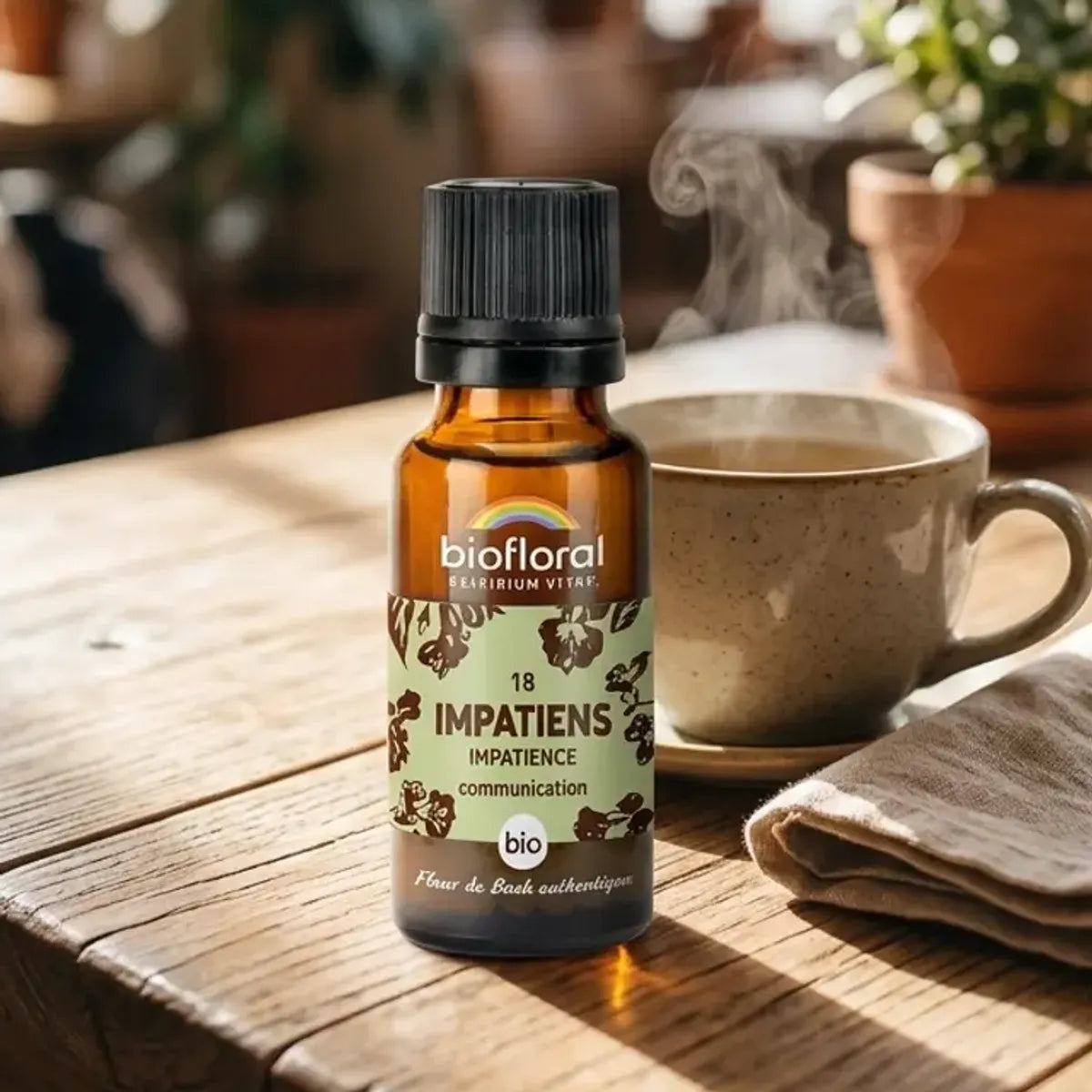 Flacon en verre ambré Fleur de Bach Impatiens Bio Biofloral sur table en bois, avec tisane et lumière douce