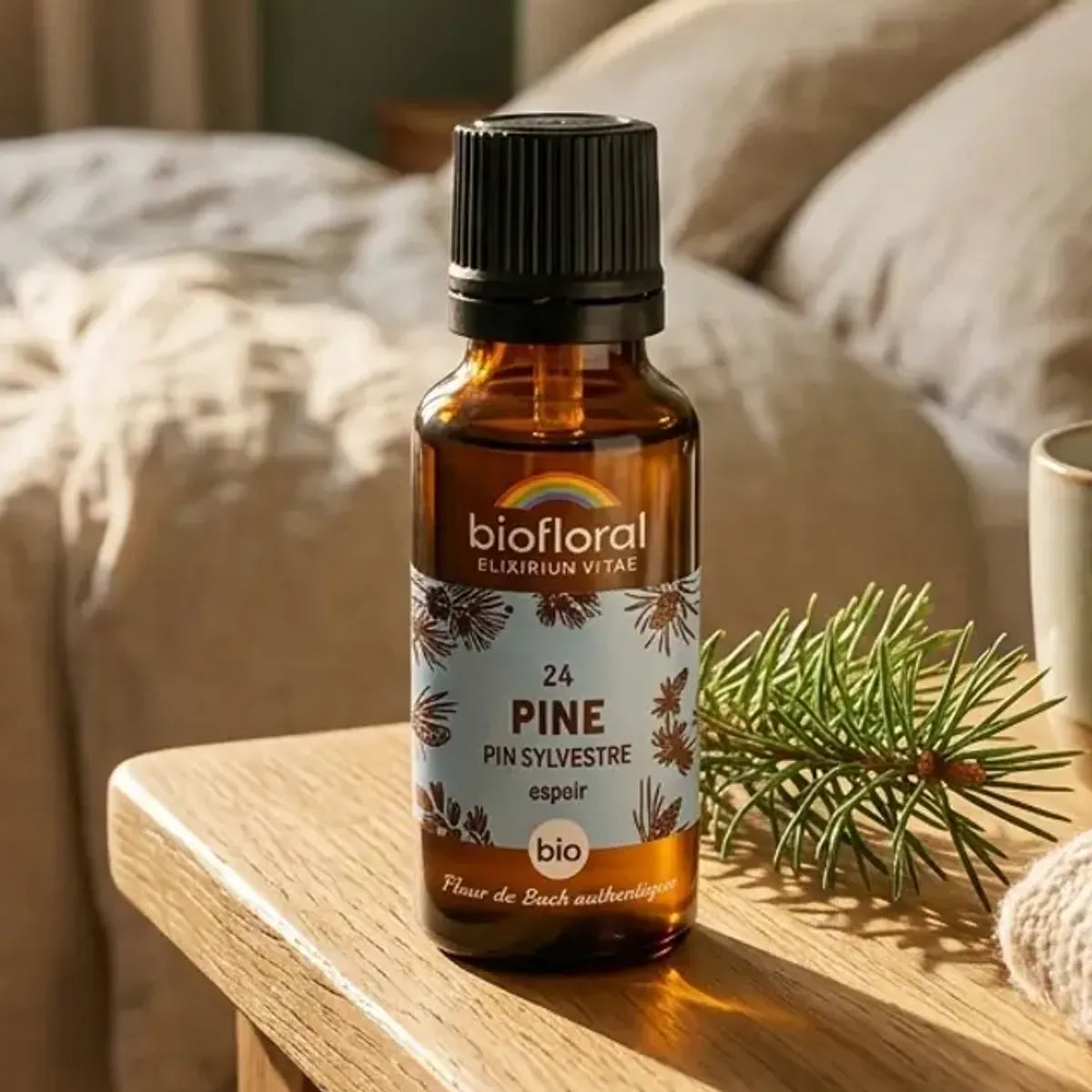 Flacon compte-gouttes ambré de Fleur de Bach Pine bio (pin sylvestre) avec étiquette bleue, posé sur une table de chevet ensoleillée