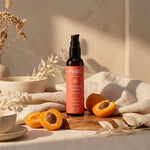 Huile d'abricot bio Najel en flacon avec pompe, entourée d'abricots frais et textiles beige