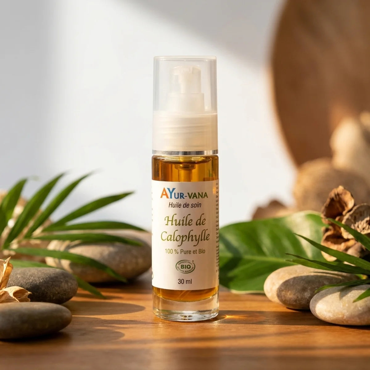 Bouteille Huile de Calophylle Bio Ayurvana sur fond spa avec feuilles tropicales et pierres lisses