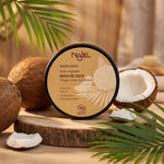 Huile de coco bio Najel en pot noir avec étiquette beige entourée de noix de coco fraîches et feuilles tropicales