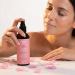 Femme vaporisant l'hydrolat de rose Najel bio sur son visage lumineux, pétales de rose