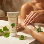 Application du lait corps Centella bio Ayurvana sur une peau hydratée avec feuilles de centella frais