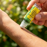 Roll-On après piqûres bio MoustiCare en application sur bras, ambiance estivale jardin