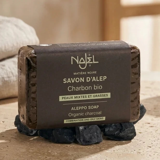 Savon d'Alep Charbon Végétal Bio Najel sur morceaux de charbon, fond blanc minimaliste