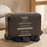 Savon d'Alep Charbon Végétal Bio Najel sur morceaux de charbon, fond blanc minimaliste