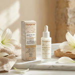 Sérum anti-âge bio 5-en-1 Florame dans son flacon compte-gouttes sur marbre blanc avec fleurs