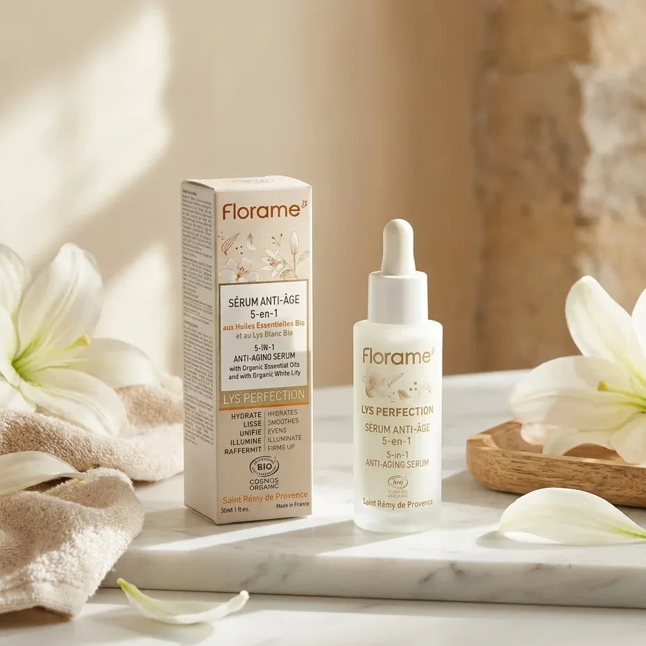 Sérum anti-âge bio 5-en-1 Florame dans son flacon compte-gouttes sur marbre blanc avec fleurs