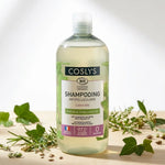 Shampooing antipelliculaire bio Coslys sur surface bois avec feuilles de lierre