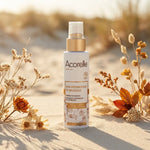 Spray bronzage certifié bio Acorelle sur surface sablée avec fleurs séchées et lumière naturelle