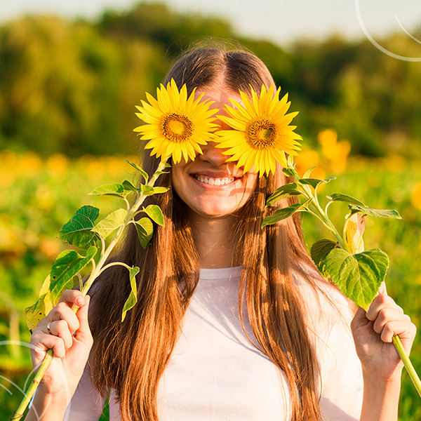 Photo d'une femme dans un champs qui a deux tournesols sur les yeux