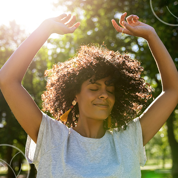 Photo d'une femme dans la nature les bras levés et qui profite du soleil