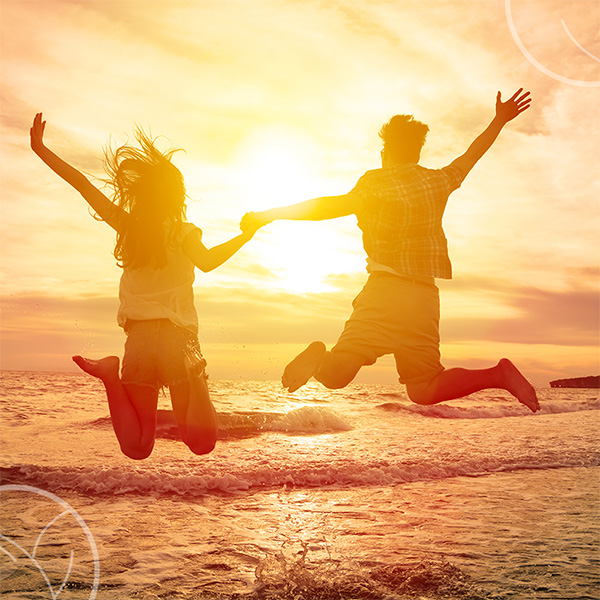 Photo d'un couple sur la plage de dos sautant en l'air en face d'un coucher de soleil